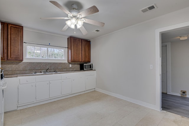 kitchen with stainless steel microwave, ornamental molding, visible vents, and a sink