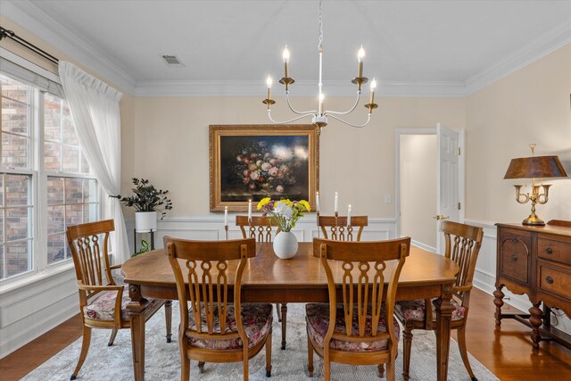 dining room with crown molding, a chandelier, wood finished floors, a decorative wall, and a wainscoted wall