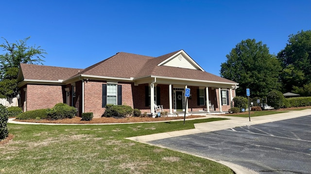 view of front of house featuring brick siding, a porch, a front yard, and uncovered parking