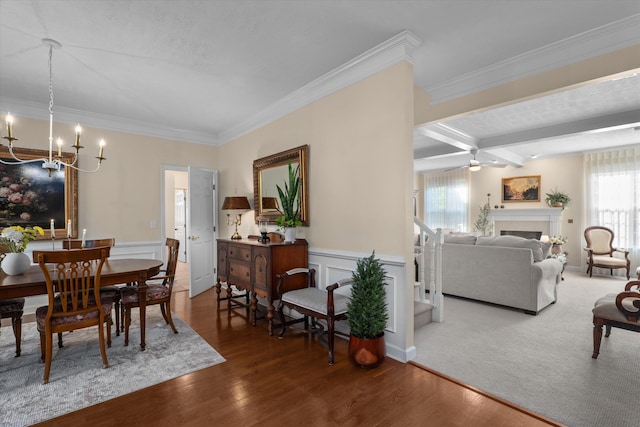 dining space featuring a chandelier, crown molding, a fireplace, wood finished floors, and a wainscoted wall