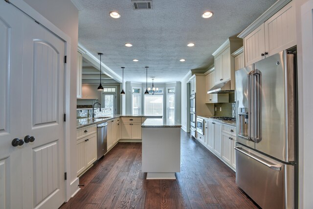 kitchen featuring pendant lighting, a center island, light stone counters, kitchen peninsula, and stainless steel appliances