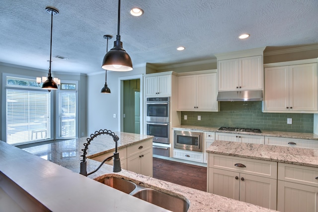 kitchen with decorative backsplash, a textured ceiling, stainless steel appliances, sink, and pendant lighting