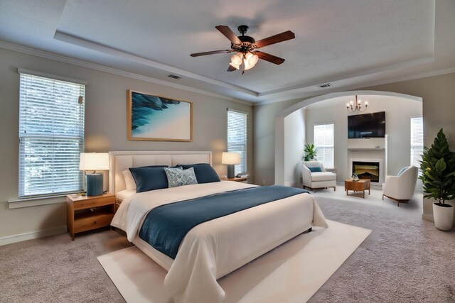 carpeted bedroom with ceiling fan with notable chandelier, multiple windows, and a tray ceiling