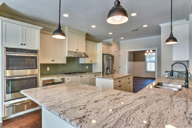 kitchen featuring appliances with stainless steel finishes, light stone counters, sink, a kitchen island, and hanging light fixtures