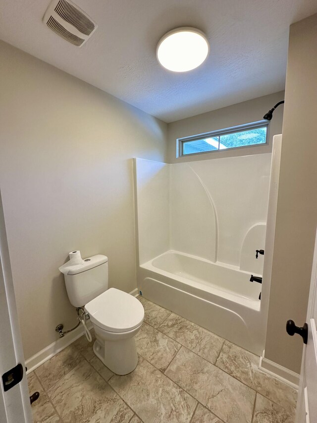 bathroom featuring washtub / shower combination, a textured ceiling, and toilet