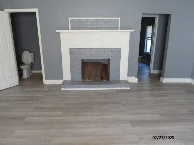 unfurnished living room featuring a brick fireplace, wood finished floors, and baseboards