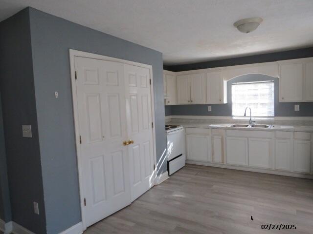 kitchen featuring white electric range oven, light wood-style flooring, light countertops, white cabinetry, and a sink