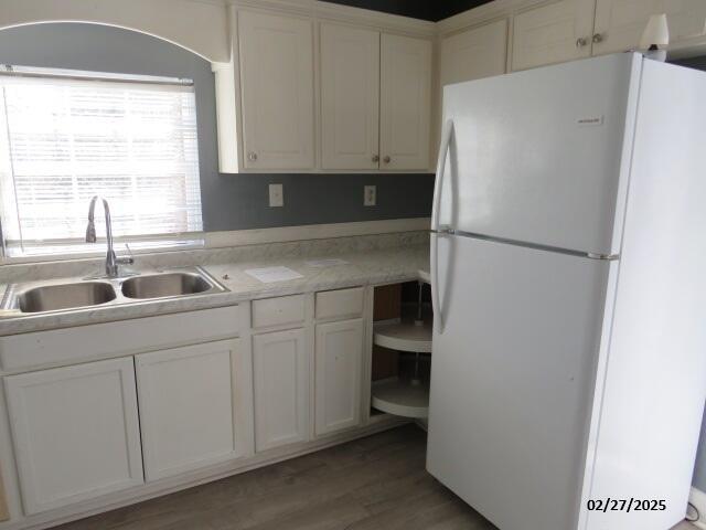 kitchen featuring light wood finished floors, white cabinets, freestanding refrigerator, light countertops, and a sink