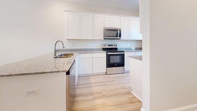 kitchen with sink, appliances with stainless steel finishes, white cabinetry, light stone countertops, and kitchen peninsula