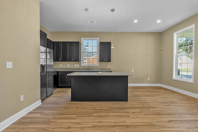 kitchen featuring a center island, sink, stainless steel fridge, decorative light fixtures, and light hardwood / wood-style floors