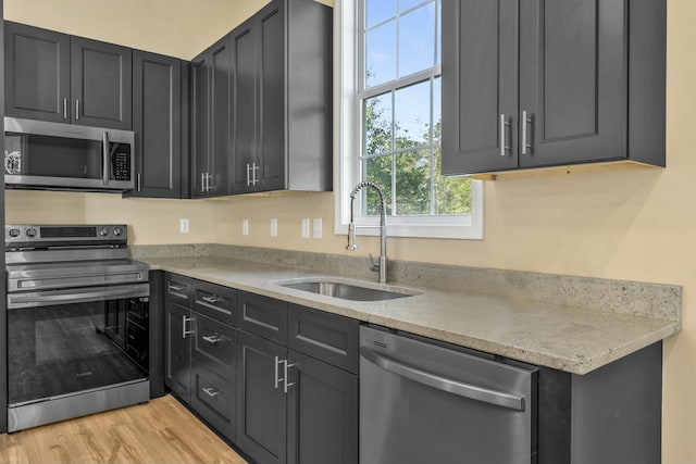 kitchen featuring appliances with stainless steel finishes, light wood-type flooring, light stone counters, and sink