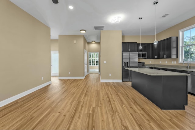 kitchen with light stone countertops, stainless steel appliances, pendant lighting, light hardwood / wood-style floors, and a kitchen island