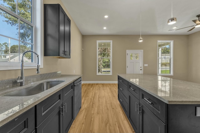 kitchen with light stone countertops, sink, dishwasher, hanging light fixtures, and light wood-type flooring