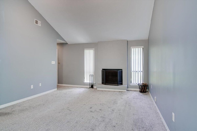 unfurnished living room featuring carpet, vaulted ceiling, and plenty of natural light