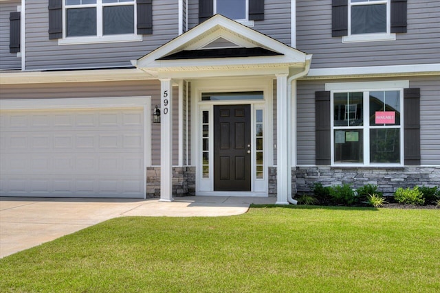 entrance to property with stone siding, a yard, an attached garage, and driveway