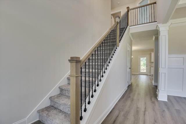 stairs featuring a high ceiling, wood finished floors, decorative columns, and baseboards