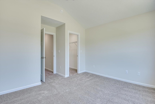 unfurnished bedroom featuring baseboards, lofted ceiling, carpet, a walk in closet, and a closet