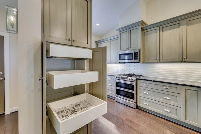 kitchen with dark wood-type flooring, stainless steel appliances, tasteful backsplash, light stone counters, and vaulted ceiling