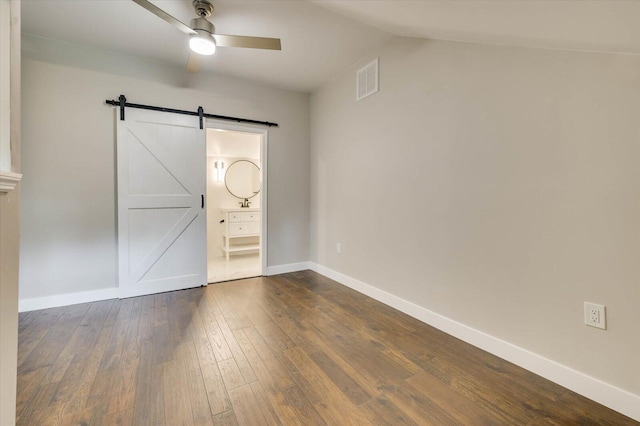 unfurnished bedroom with connected bathroom, ceiling fan, dark wood-type flooring, a barn door, and lofted ceiling