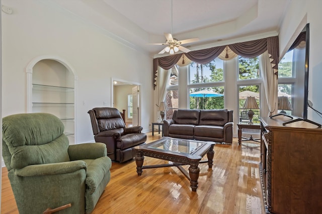 living room featuring a tray ceiling, ceiling fan, built in features, and light wood-type flooring