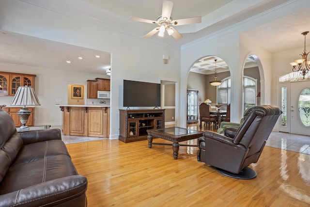 living room with ceiling fan with notable chandelier, light hardwood / wood-style flooring, and ornamental molding