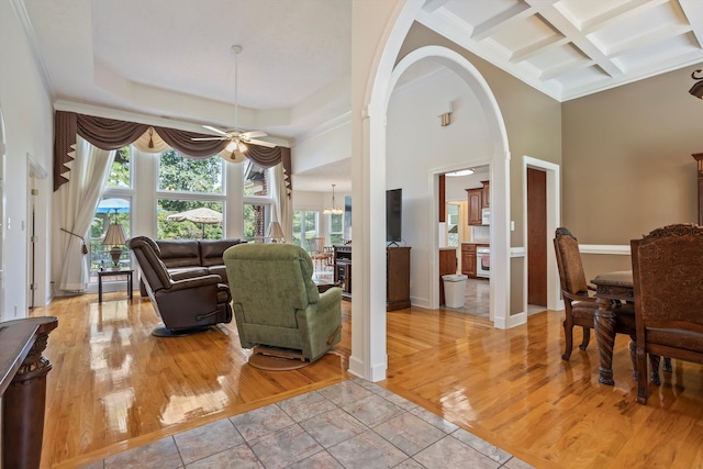 living room featuring beamed ceiling, light tile patterned floors, ceiling fan with notable chandelier, and coffered ceiling