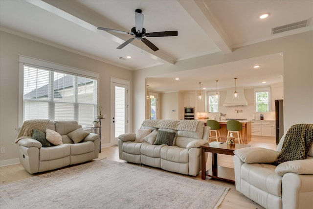 living area with light wood-style flooring, a ceiling fan, recessed lighting, visible vents, and ornamental molding