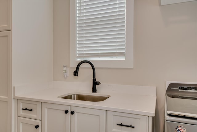 kitchen with a sink, washer / dryer, white cabinetry, and light countertops