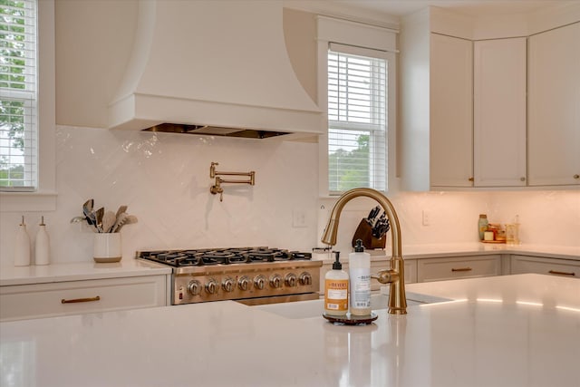kitchen featuring backsplash, stove, light countertops, premium range hood, and white cabinetry