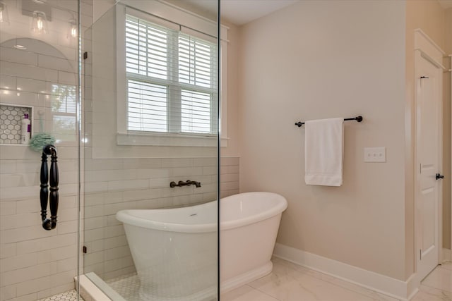 full bathroom featuring baseboards, marble finish floor, a freestanding tub, and tiled shower