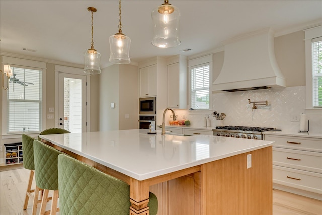 kitchen with a kitchen island with sink, oven, premium range hood, light wood-type flooring, and built in microwave
