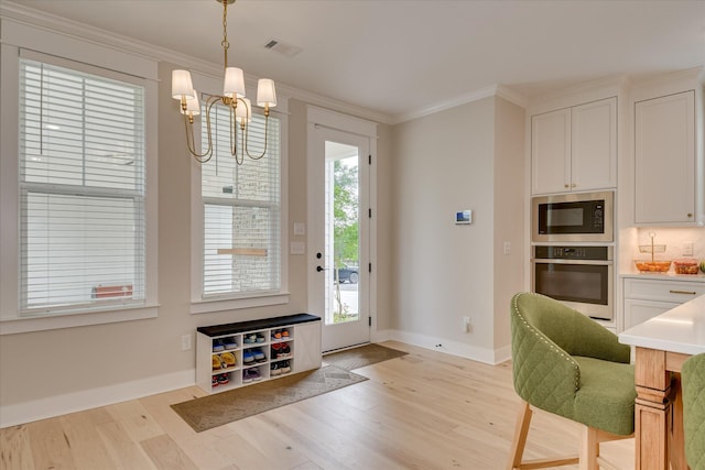 doorway featuring an inviting chandelier, ornamental molding, light wood finished floors, and visible vents