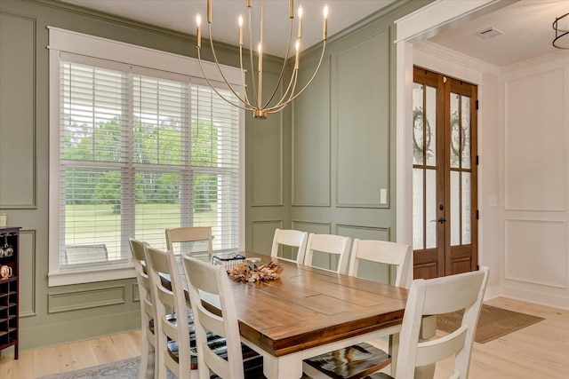 dining area with french doors, an inviting chandelier, ornamental molding, a decorative wall, and light wood-style flooring