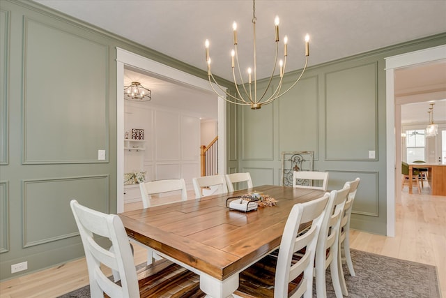 dining area featuring light wood-type flooring, ornamental molding, a decorative wall, and a chandelier