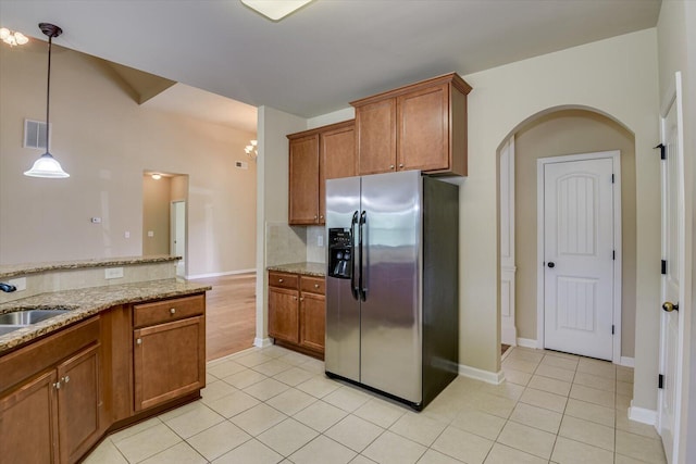 kitchen featuring light stone countertops, sink, stainless steel refrigerator with ice dispenser, pendant lighting, and light tile patterned flooring