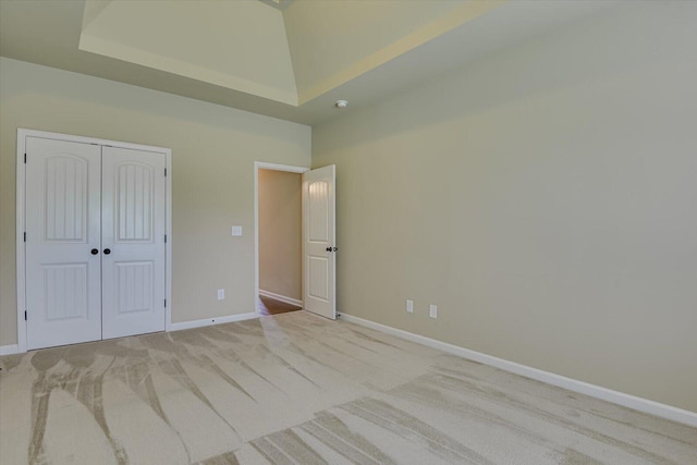 unfurnished bedroom with a high ceiling, light colored carpet, a closet, and a tray ceiling