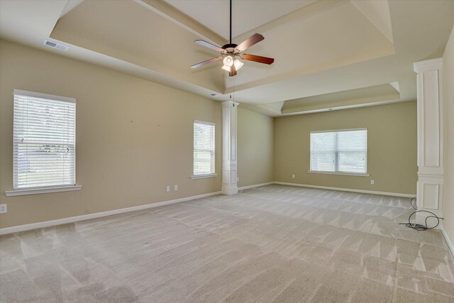 carpeted empty room featuring a tray ceiling, decorative columns, a healthy amount of sunlight, and ceiling fan