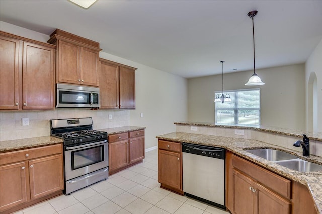 kitchen with decorative backsplash, appliances with stainless steel finishes, light stone counters, sink, and decorative light fixtures