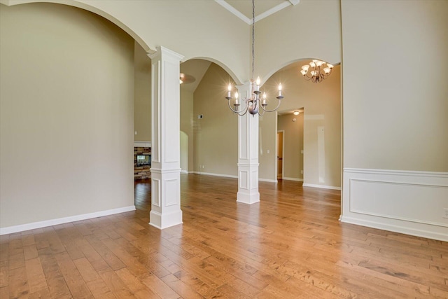 spare room featuring a chandelier, decorative columns, hardwood / wood-style flooring, and crown molding