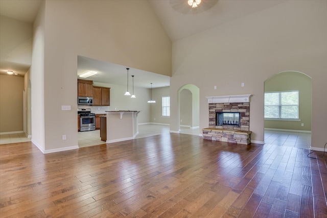 unfurnished living room with a fireplace, light hardwood / wood-style flooring, high vaulted ceiling, and ceiling fan