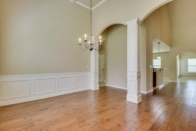 spare room with decorative columns, wood-type flooring, a notable chandelier, and ornamental molding