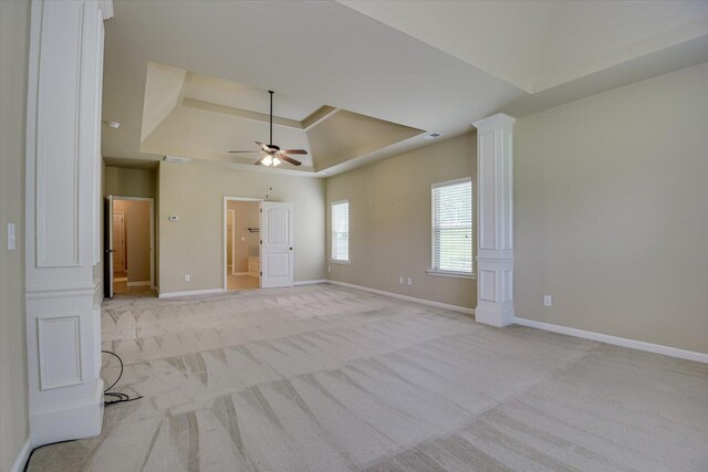 empty room with a raised ceiling, light carpet, and ceiling fan