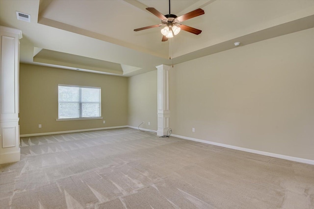 carpeted spare room with ceiling fan, ornate columns, and a tray ceiling