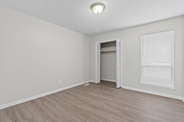 unfurnished bedroom featuring a textured ceiling, a closet, and light hardwood / wood-style flooring