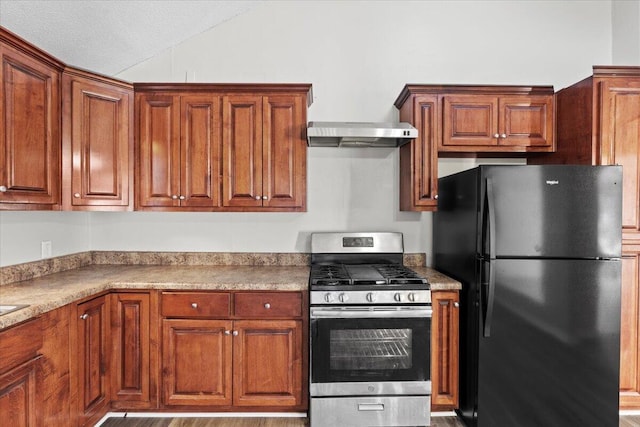 kitchen featuring stainless steel gas range, a textured ceiling, light hardwood / wood-style flooring, black fridge, and wall chimney range hood