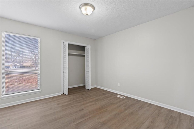 unfurnished bedroom with a textured ceiling, a closet, and hardwood / wood-style flooring