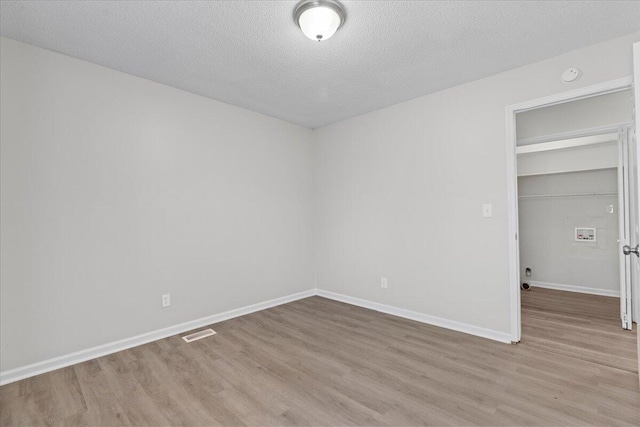 unfurnished bedroom featuring a textured ceiling, a closet, and light hardwood / wood-style flooring