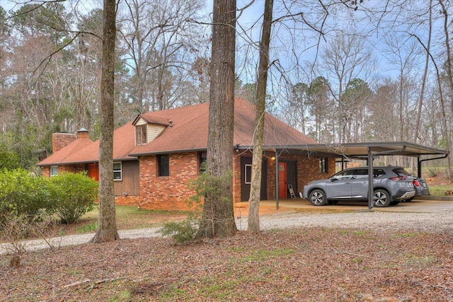 view of side of property with driveway, an attached carport, roof with shingles, brick siding, and a chimney