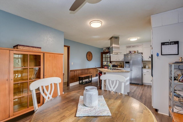 dining area featuring wood walls, wainscoting, wood finished floors, a textured ceiling, and a ceiling fan