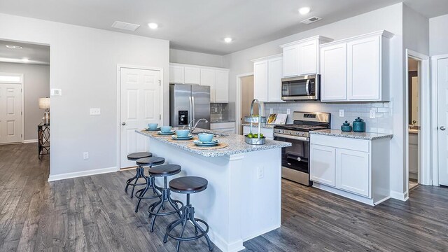 kitchen featuring tasteful backsplash, dark hardwood / wood-style floors, a center island with sink, white cabinets, and appliances with stainless steel finishes